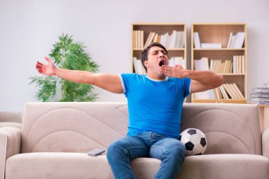 Evdeki kanepede oturup futbol izleyen bir adam.