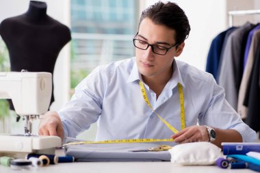 Genç terzi yeni elbiseler üzerinde çalışıyor.
