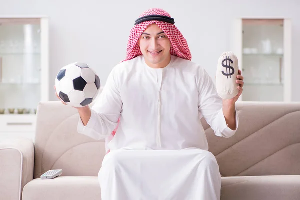 Young arab man watching football sitting on sofa