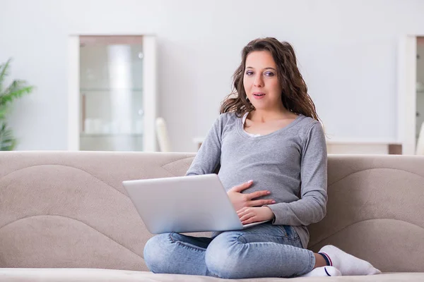 Schwangere arbeitet am Laptop und sitzt auf Sofa — Stockfoto