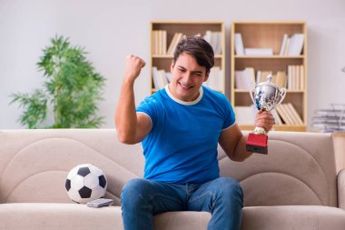 Evdeki kanepede oturup futbol izleyen bir adam.