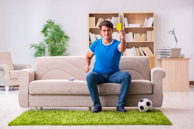 Evdeki kanepede oturup futbol izleyen bir adam.