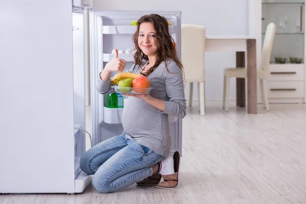 Беременная женщина возле холодильника ищет еду и закуски — стоковое фото