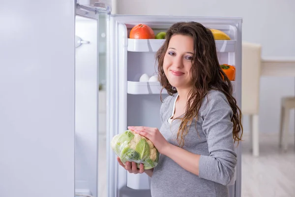 Zwangere vrouw in de buurt koelkast op zoek naar voedsel en snacks — Stockfoto