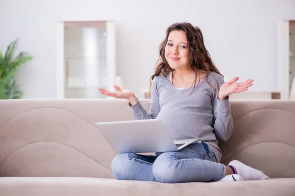 Femme enceinte travaillant sur un ordinateur portable assis sur un canapé — Photo