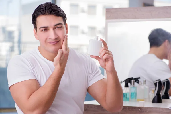 Joven hombre guapo aplicando crema facial —  Fotos de Stock