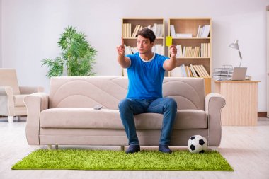 Evdeki kanepede oturup futbol izleyen bir adam.
