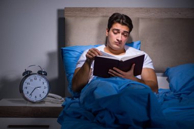 Genç adam yatakta kitap okuyor.