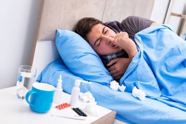 Grip olmuş hasta adam yatakta yatıyor.