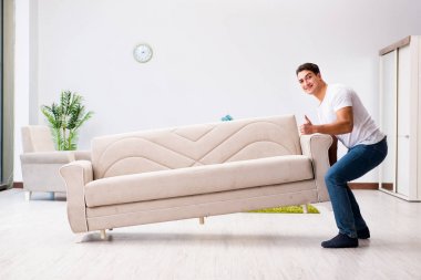 Genç adam evde mobilya taşıyor.