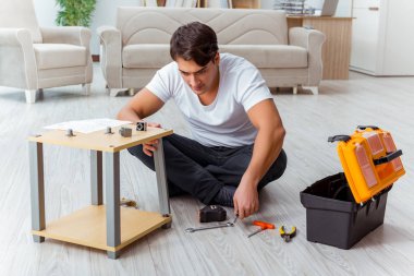 Adam evde mobilya montajı yapıyor.