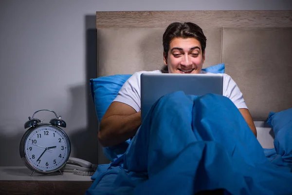 Young man working on laptop in bed — Stock Photo, Image