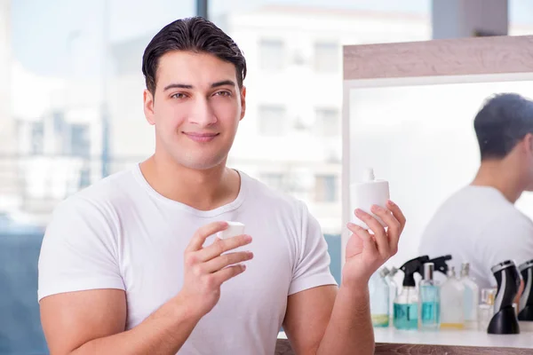 Jovem homem bonito aplicando creme facial — Fotografia de Stock