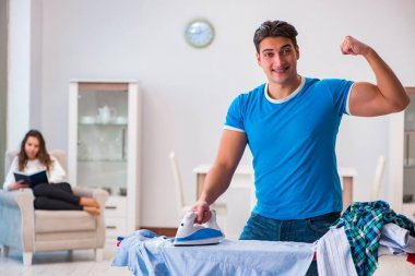 Erkek koca evde ütü yapıyor, karısına yardım ediyor.