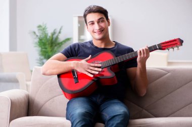 Genç adam evde gitar çalıyor.
