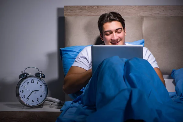 Young man working on laptop in bed — Stock Photo, Image