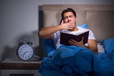 Genç adam yatakta kitap okuyor.