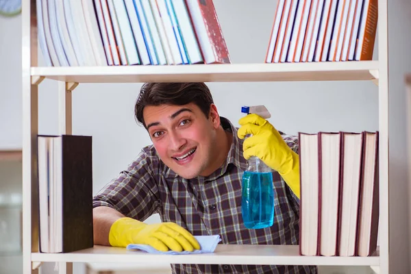 Muž čistí prach z police na knihy — Stock fotografie