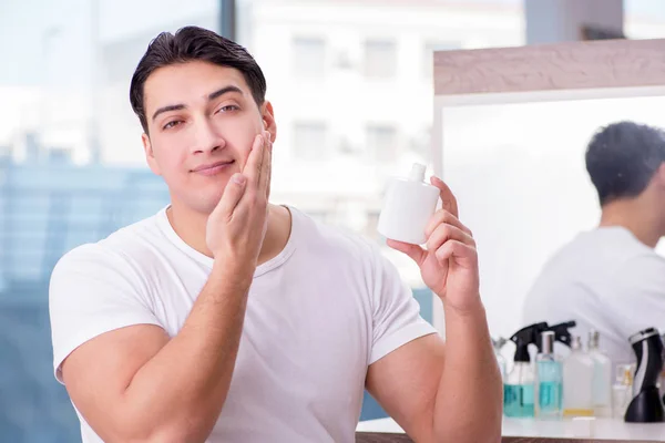 Jovem homem bonito aplicando creme facial — Fotografia de Stock