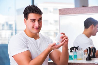 Genç yakışıklı adam yüz kremi sürüyor.