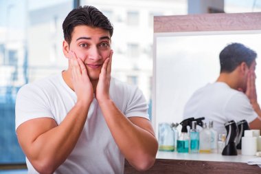 Genç yakışıklı adam yüz kremi sürüyor.