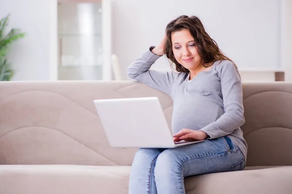 Schwangere arbeitet am Laptop und sitzt auf Sofa — Stockfoto