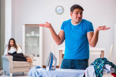 Erkek koca evde ütü yapıyor, karısına yardım ediyor.