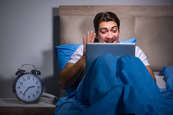 Young man working on laptop in bed — Stock Photo, Image