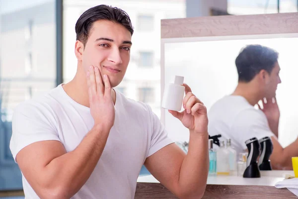 Jovem homem bonito aplicando creme facial — Fotografia de Stock