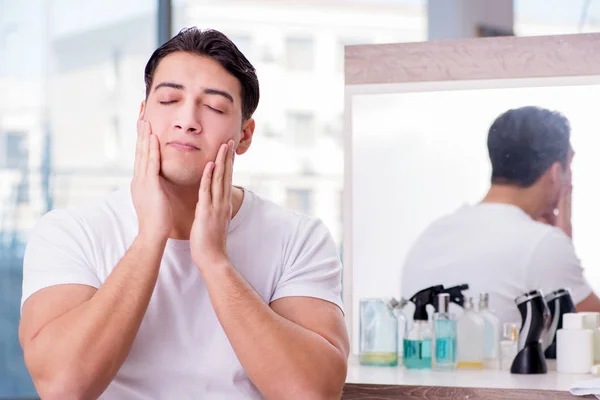 Jovem homem bonito aplicando creme facial — Fotografia de Stock