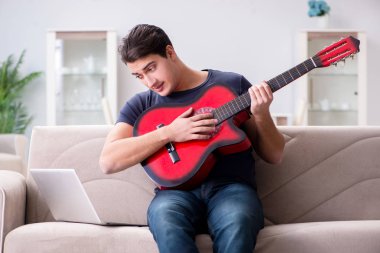 Genç adam evde gitar çalıyor.