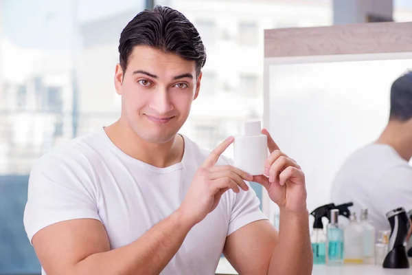 Jovem homem bonito aplicando creme facial — Fotografia de Stock