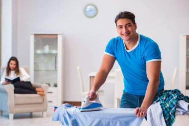 Erkek koca evde ütü yapıyor, karısına yardım ediyor.