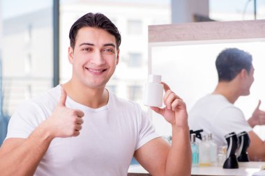 Genç yakışıklı adam yüz kremi sürüyor.