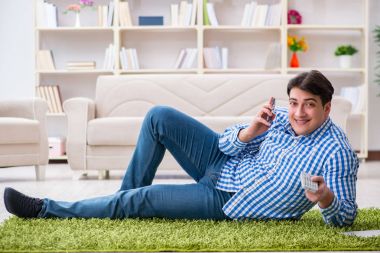 Genç yakışıklı adam evde yerde oturuyor.