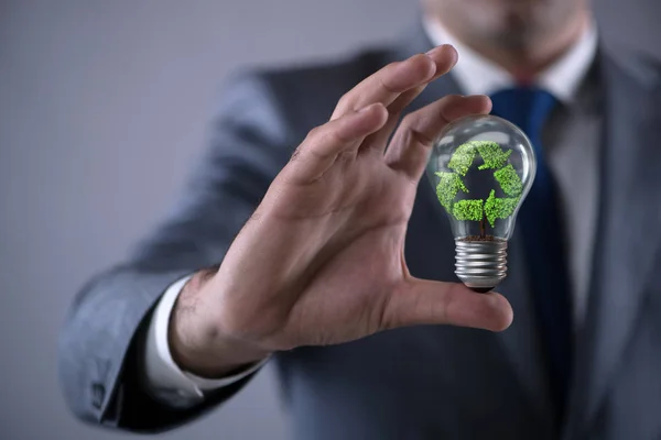 Бизнесмен держит лампу в зеленой среде концепции — стоковое фото