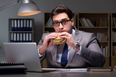 Gece geç saatte iş adamı hamburger yiyor.