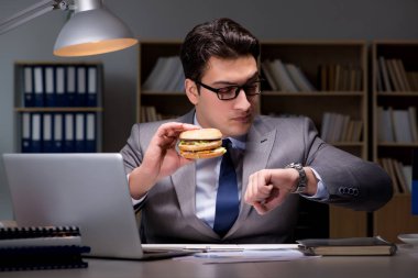Gece geç saatte iş adamı hamburger yiyor.