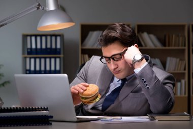 Gece geç saatte iş adamı hamburger yiyor.