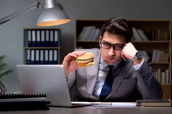 Empresário tarde da noite comendo um hambúrguer — Fotografia de Stock