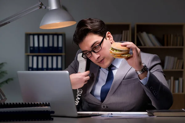 Uomo d'affari a tarda notte mangiare un hamburger — Foto Stock