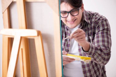 Genç erkek sanatçı parlak stüdyoda resimler çiziyor.