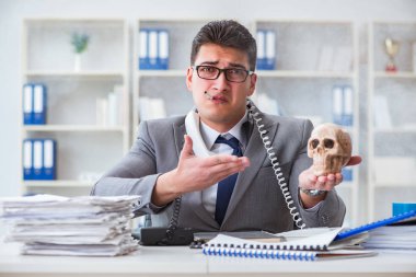 Ofisteki işadamı elinde insan kafatasıyla sigara içiyor.