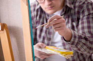 Genç erkek sanatçı parlak stüdyoda resimler çiziyor.