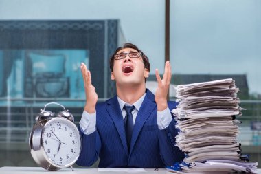 Yığınla evrak işi ve alarm sistemi olan bir iş adamı.