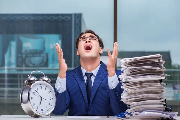 Yığınla evrak işi ve alarm sistemi olan bir iş adamı.