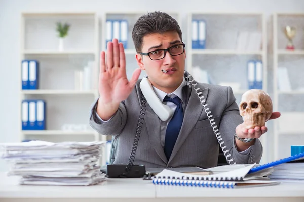 Ofisteki işadamı elinde insan kafatasıyla sigara içiyor.