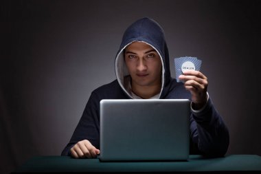 Kapüşonlu genç adam dizüstü bilgisayarın önünde oturuyor.