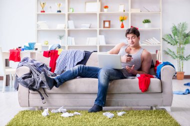 Genç adam dağınık bir odada çalışıyor.