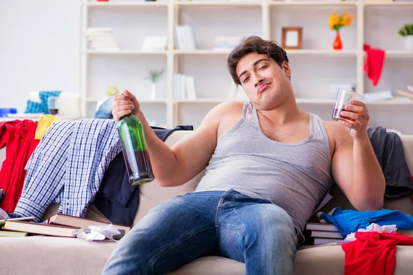 Jongeman student dronken alcohol drinken in een rommelige kamer — Stockfoto